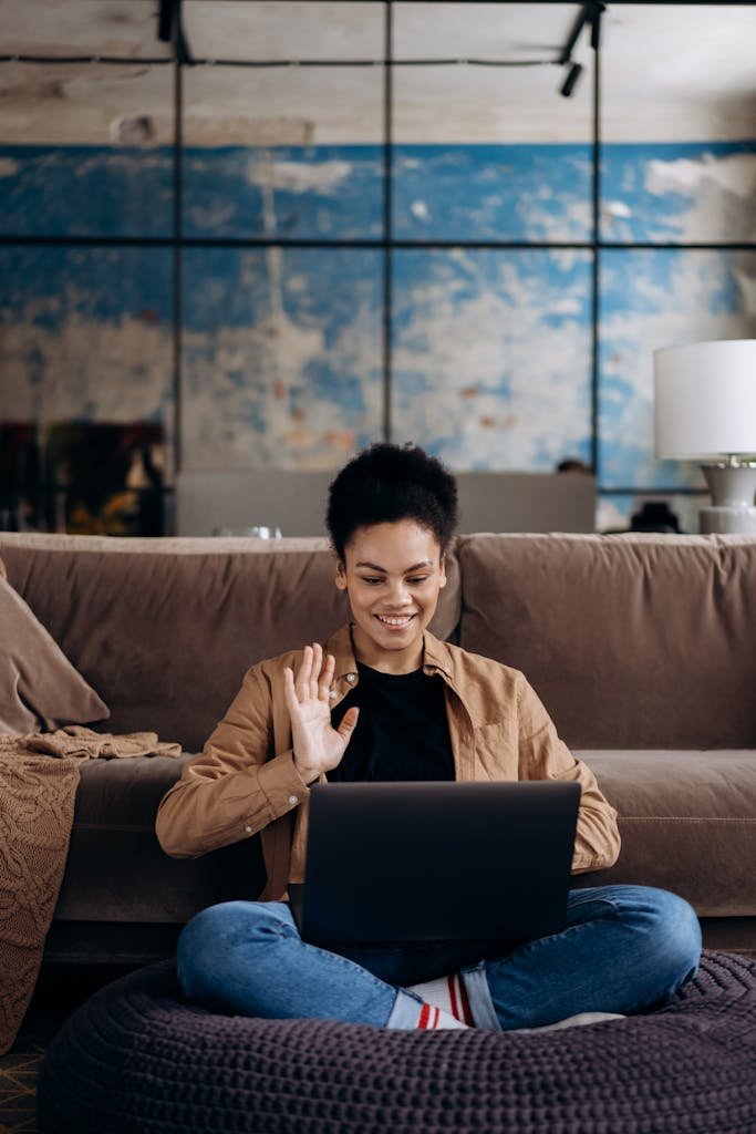 A young woman enjoys a video call on her laptop in a cozy home setting, showcasing remote work flexibility.